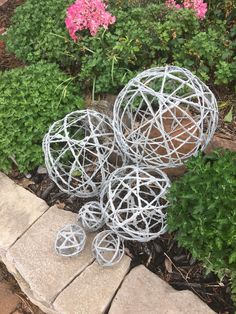 three metal balls sitting on top of a stone walkway in front of some plants and flowers