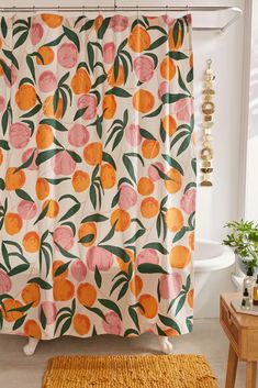 a shower curtain with oranges and leaves on it in a white bathroom next to a yellow rug