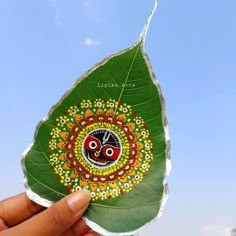 a person holding up a green leaf with an artistic design on it's side