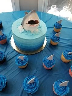 a blue table with cupcakes and a shark cake