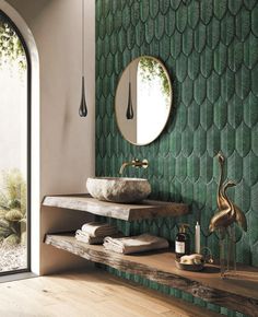 a bathroom with green tiles on the wall and wooden flooring, along with a round mirror