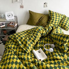 an unmade bed with yellow and green checkered comforter, headphones on the pillow