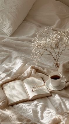 a cup of coffee and an open book on a bed with white linens,