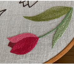 a close up of a cross stitch pattern with a flower on the bottom and green leaves