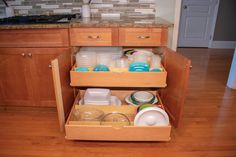 an open drawer in a kitchen with dishes and cups on the bottom shelf next to it