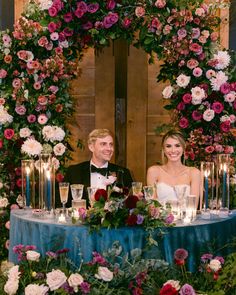 a man and woman sitting at a table with flowers on it, surrounded by candles