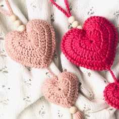 two crocheted heart ornaments are laying on a white blanket, one is pink and the other is red