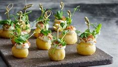 small appetizers are arranged on top of a slate slab with green garnish