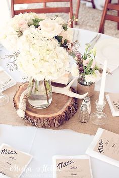 the table is set with flowers in vases and place cards for guests to use