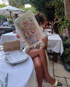 a woman sitting at a table holding up a framed print in front of her face