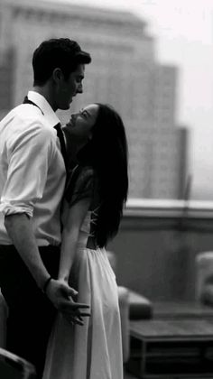 a man and woman standing next to each other on top of a roof in front of tall buildings