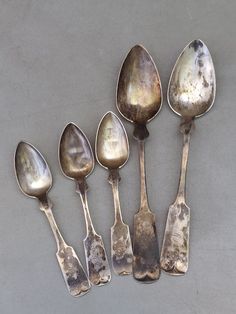 six old spoons are lined up in a row on a gray surface with white spots