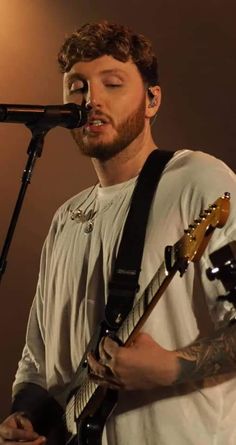 a man that is standing in front of a microphone with his eyes closed while playing an electric guitar