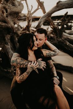 a man and woman hugging each other in front of some driftwood at the beach