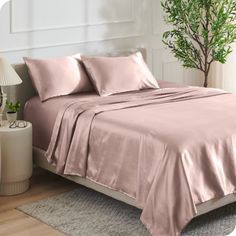 a bed with pink sheets and pillows in a room next to a plant on the floor