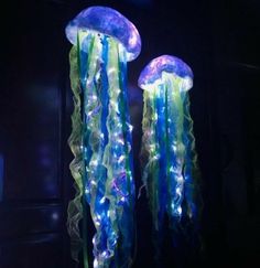 two blue and green jellyfish lights hanging from the side of a wall in a dark room