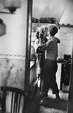 black and white photograph of two people standing in a kitchen, one holding the other's head