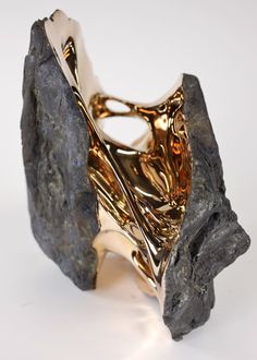 a gold and silver object sitting on top of a white table next to a black rock