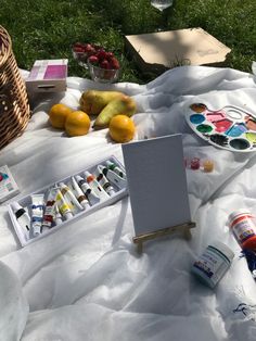 an easel, paintbrushes and other items on a blanket in the grass