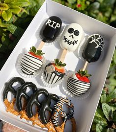 an assortment of halloween treats in a white box with strawberries and pretzels