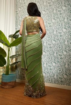 Editor's Note Perfect times embodies its name, crafted from a delicate georgette base, the pre-stitched sari features net pleats, sequins, and golden beaded embroidery, which are intricately done to create a stunning texture. The sari comes with a matching halter blouse in the same shade and features delicate embroidery work, which perfectly complements the design of the sari. Color: Olive green Fabric: Georgette tulle Sleeve type: Sleeveless Embroidery details: Sequins, and golden beaded embroi Embellished Saree, Green Sari, Halter Blouse, Party Attire, Tulle Sleeves, Saree Designs Party Wear, Drape Saree, Delicate Embroidery, Korean Street