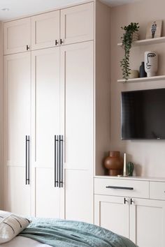 a bedroom with white cabinets and a flat screen tv mounted on the wall above it