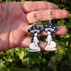 a pair of black and white earrings in the shape of a woman with mushrooms on her head