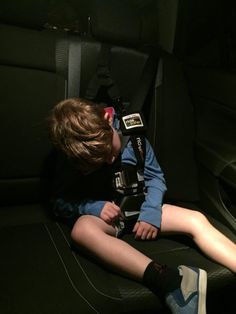 a young boy sitting in the back seat of a car with his feet up and head down