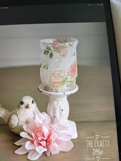 a small white bird sitting next to a candle holder with a pink flower on it