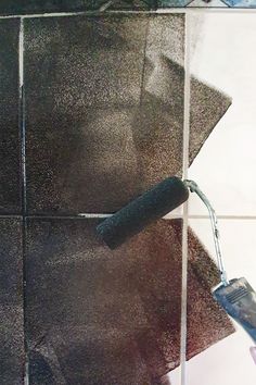 a person using a paint roller to spray paint on a tiled wall with black and white tiles