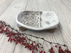 a white bowl sitting on top of a wooden table next to a branch with red berries