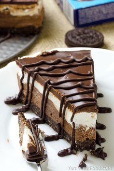 a slice of chocolate cheesecake on a white plate with a fork and oreo cookies in the background