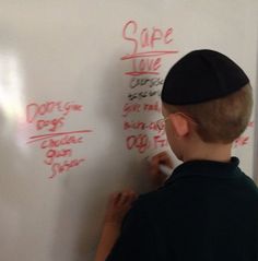 a young boy writing on a whiteboard with red marker and some words written on it