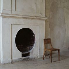 a chair sitting next to a fire place in a room with white walls and stone flooring