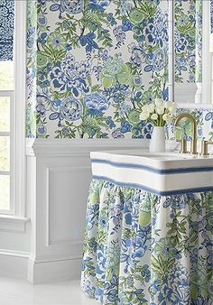 a bathroom with blue and green floral wallpaper, sink and window curtains in it