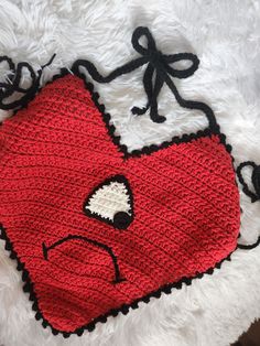 a red and black crocheted bag on top of a white furry rug with an angry face drawn on it