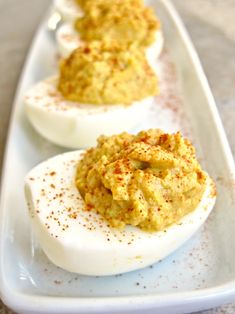 deviled eggs with mustard and seasoning sit on a white platter, ready to be eaten