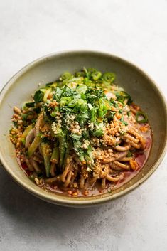 a bowl filled with noodles and vegetables on top of a white countertop next to a fork