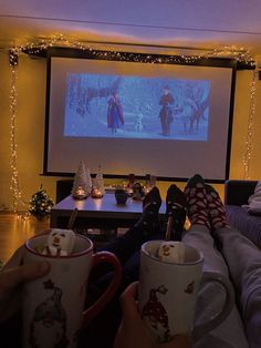 two people sitting in front of a projection screen holding coffee mugs with their feet up