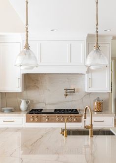 a kitchen with marble counter tops and white cabinets, two pendant lights over the stove