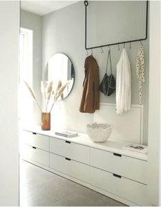 a white room with some clothes hanging on the wall and two mirrors above it,