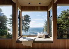 there is a window seat in front of the windows looking out at the ocean and trees