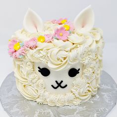 a cake with white frosting and pink flowers on top, decorated to look like an animal's head