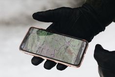 a person in black gloves holding a cell phone with a map on the back of it