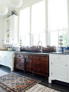 a kitchen with white cabinets and an area rug in front of the sink, along with hanging lights