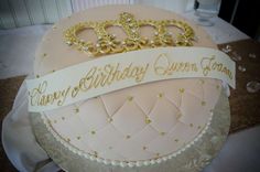 a birthday cake with a tiara and ribbon on it's top, sitting on a table