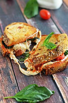 there is a sandwich on the table with spinach leaves and tomatoes in the background