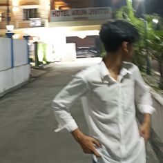 a man in white shirt and jeans walking down the street at night with his hands on his hips