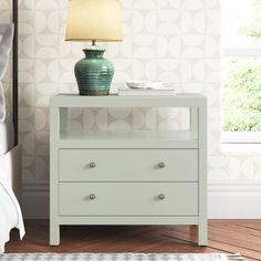 a nightstand with a lamp on top of it next to a bed