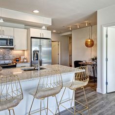 a kitchen with white cabinets and marble counter tops, two bar stools in front of the island